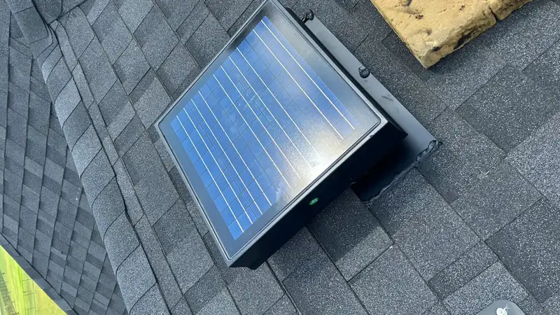 Solar attic fan installed on a shingle roof next to a valley